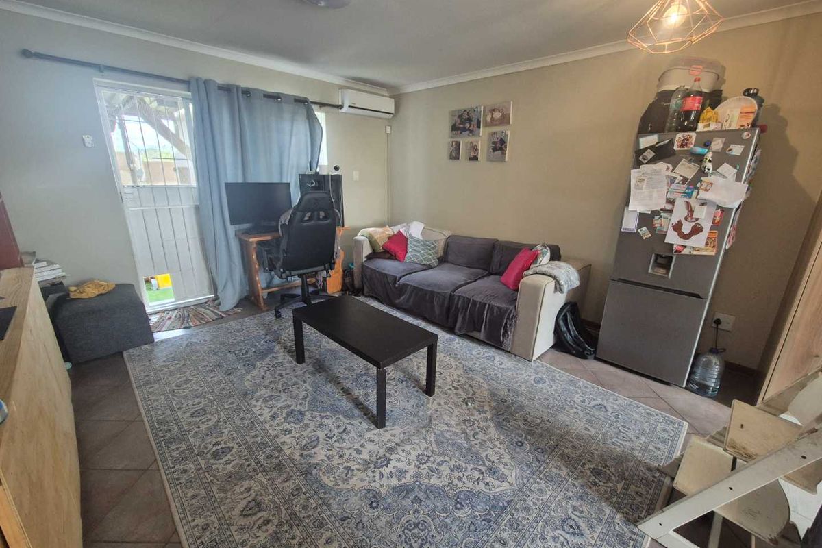 A functional living room featuring tiled flooring, a split-system air conditioner, and direct access to an outdoor area via a security gate.