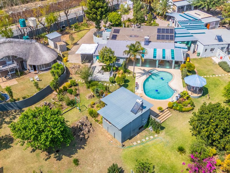 Aerial view of a small holding property featuring multiple buildings, a swimming pool, a gazebo, solar panels, and extensive landscaped garden areas.
