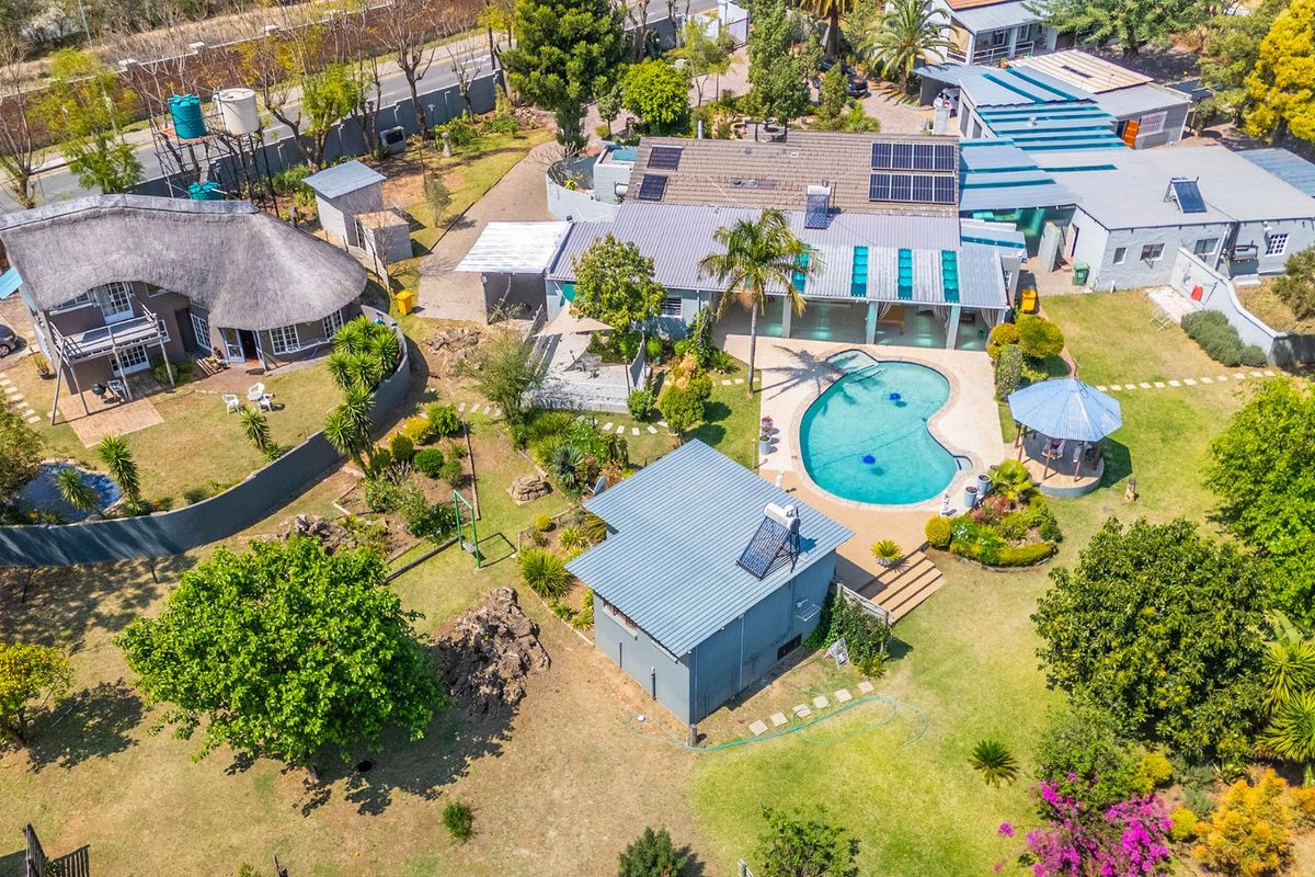 Aerial view of a small holding property featuring multiple buildings, a swimming pool, a gazebo, solar panels, and extensive landscaped garden areas.