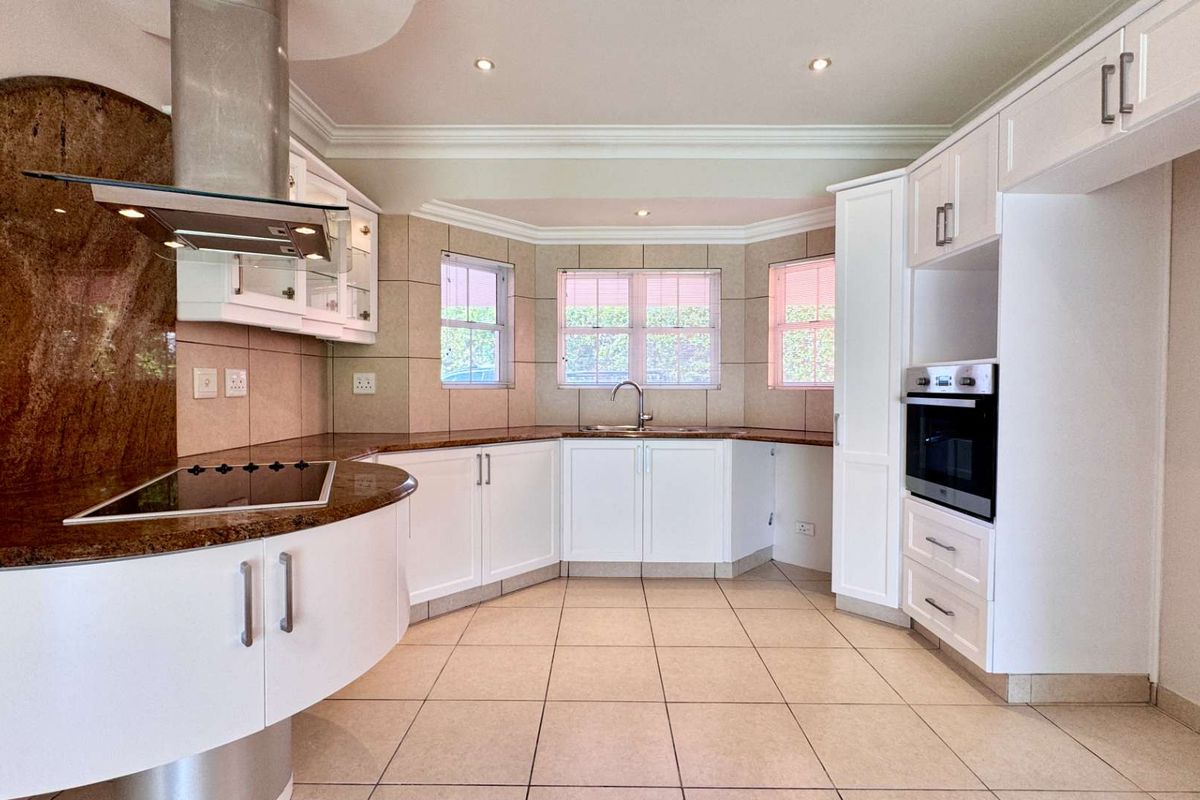 A spacious, well-maintained kitchen featuring white cabinetry, granite countertops, built-in oven, electric hob, and tiled flooring with ample natural light.