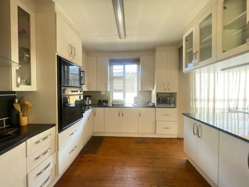 A functional kitchen featuring white cabinetry, dark countertops, built-in oven, and warm timber flooring, offering a classic and practical layout.