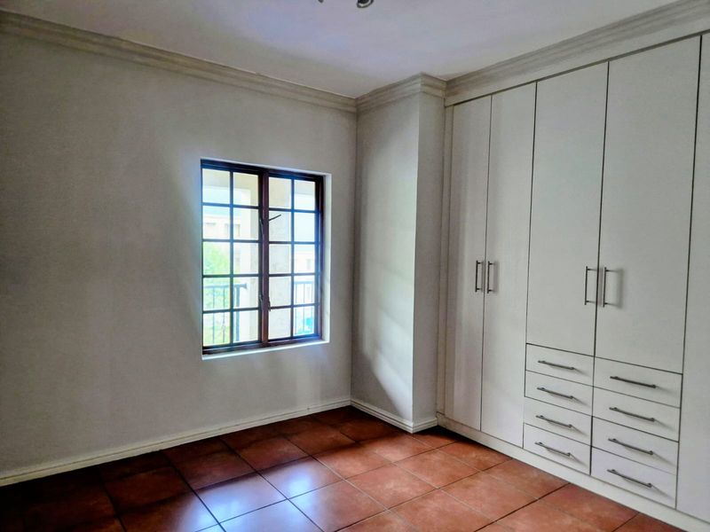 An empty bedroom featuring tiled flooring, built-in cupboards with ample storage, and decorative ceiling cornicing.