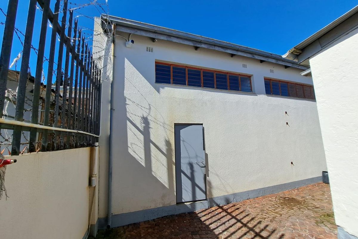 Rear exterior view of the property featuring a paved courtyard, security fencing, and a single access door with high-level windows.