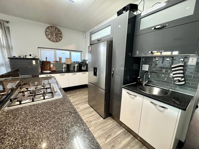 Modern kitchen featuring granite countertops, a gas hob, subway tile backsplash, and contemporary two-tone cabinetry with ample storage space.