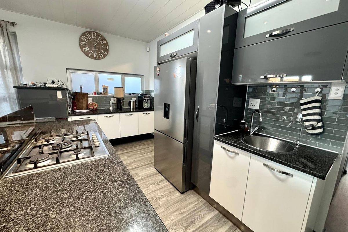 Modern kitchen featuring granite countertops, a gas hob, subway tile backsplash, and contemporary two-tone cabinetry with ample storage space.