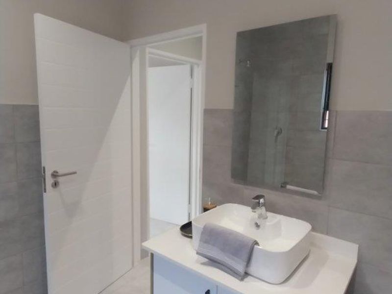 Modern bathroom featuring a sleek vanity cabinet with a vessel sink, wall-mounted mirror, and neutral grey wall and floor tiling.