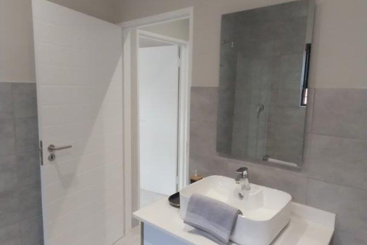 Modern bathroom featuring a sleek vanity cabinet with a vessel sink, wall-mounted mirror, and neutral grey wall and floor tiling.