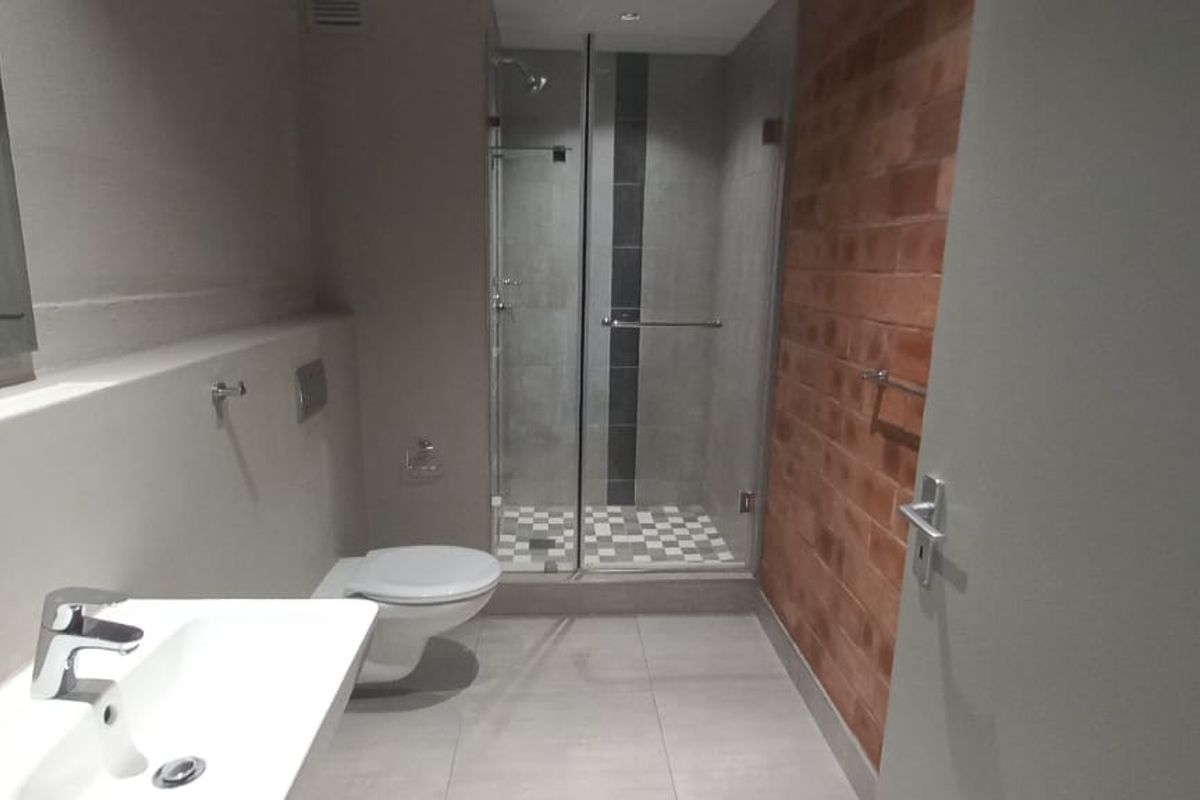 Modern bathroom featuring a glass-enclosed shower, wall-mounted toilet, contemporary basin, and a distinctive exposed brick feature wall.