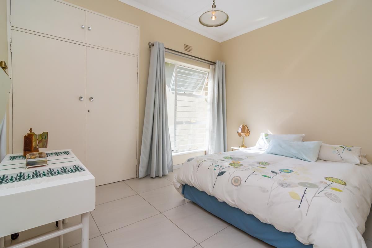 A well-lit bedroom featuring built-in cupboards, tiled flooring, and a large window with natural light.