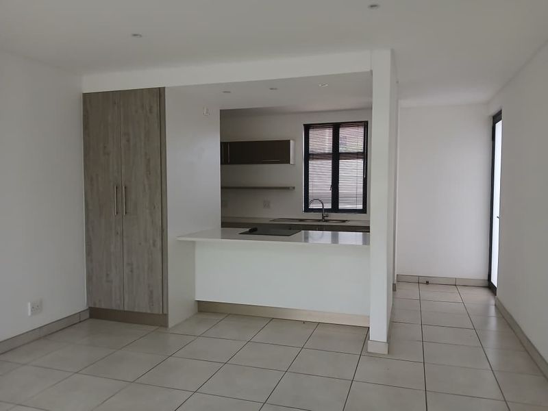 Open plan kitchen and living area featuring modern cabinetry, a central island with hob, and neutral tiled flooring throughout.