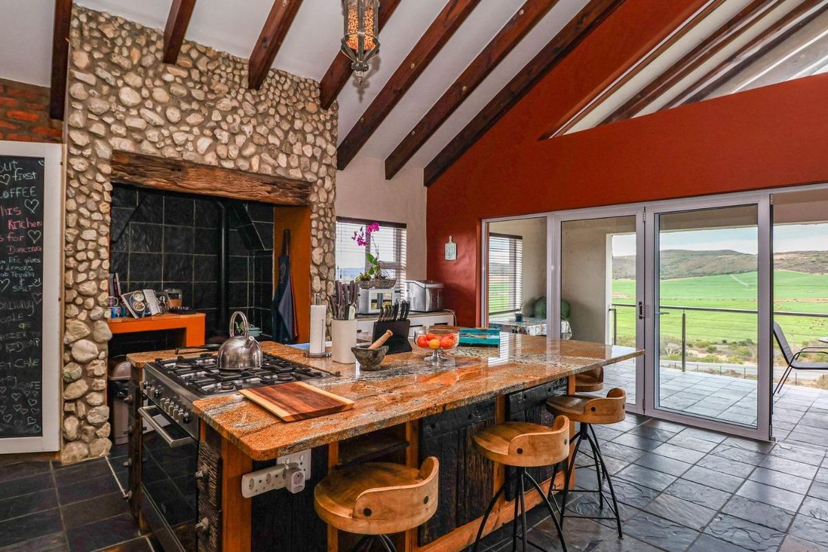 Spacious kitchen featuring a large granite-topped island, built-in gas stove, stone feature wall, exposed timber beams, and sliding doors opening to a scenic balcony.
