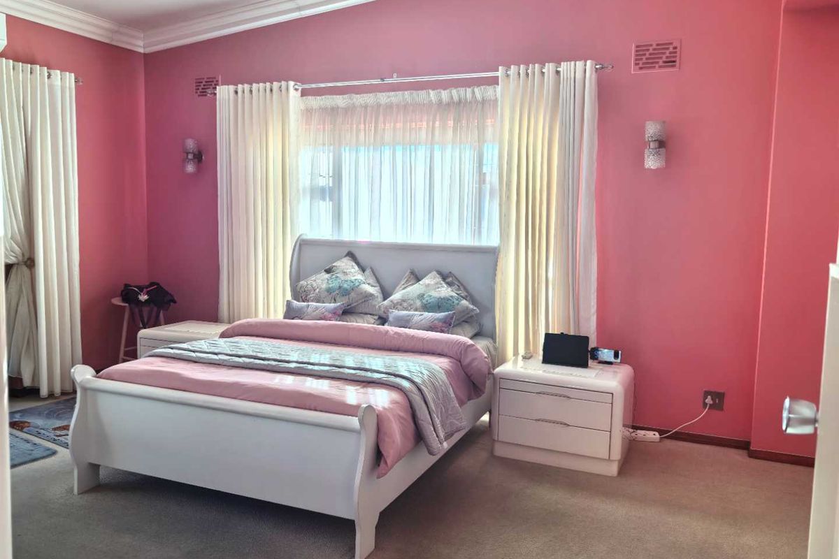 A spacious bedroom featuring neutral carpeting, crown molding, and wall-mounted light fixtures, currently finished with vibrant pink wall paint.