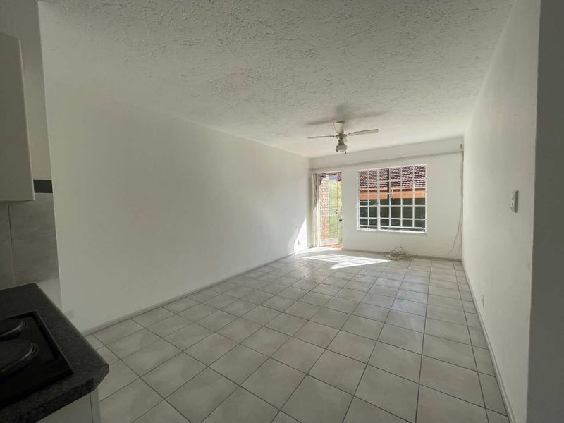 An empty open-plan living and kitchen area featuring tiled floors, a ceiling fan, and direct access to an outdoor space.