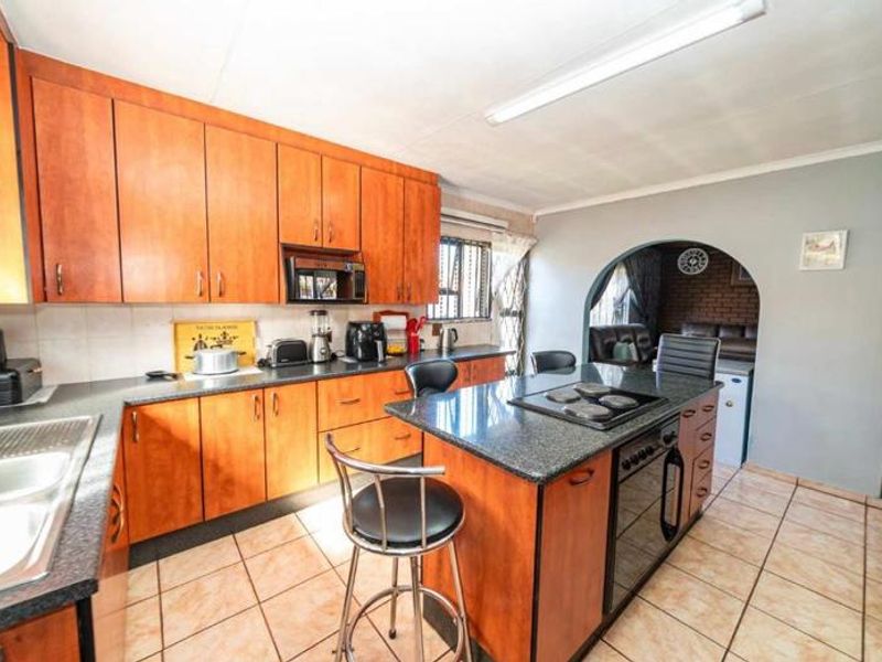 A functional kitchen featuring wooden cabinetry, granite countertops, a central island with a built-in oven and hob, and tiled flooring.