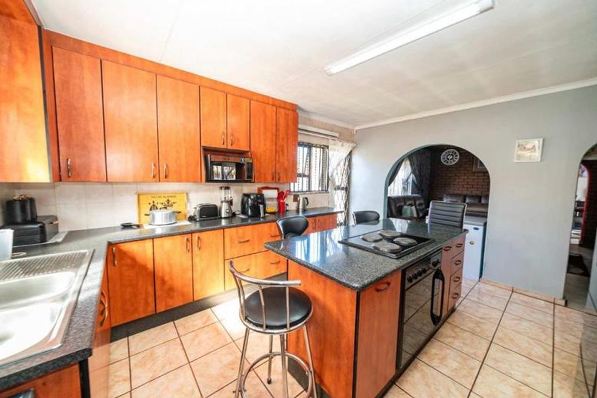 A functional kitchen featuring wooden cabinetry, granite countertops, a central island with a built-in oven and hob, and tiled flooring.