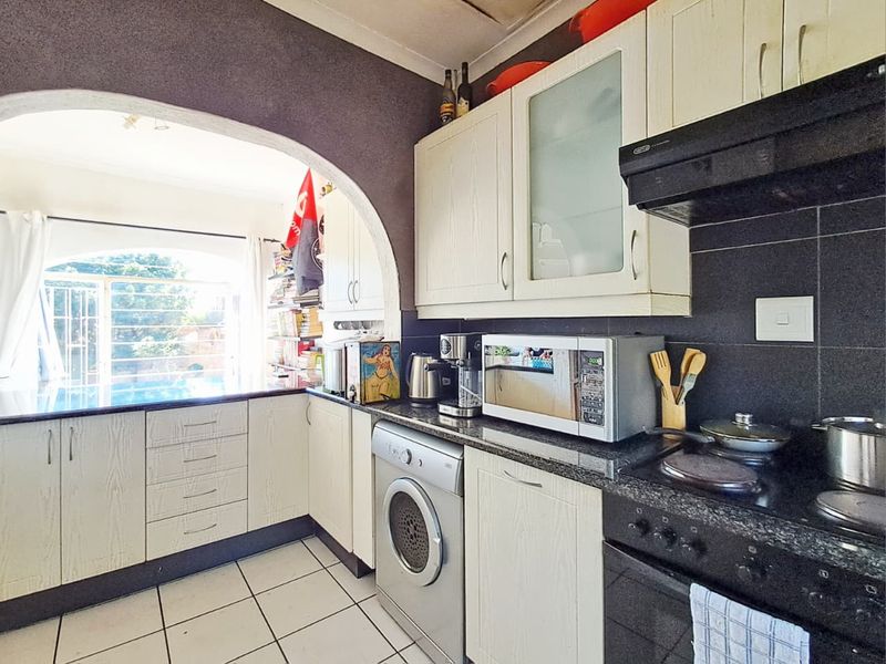 A functional kitchen featuring built-in cabinetry, granite countertops, an integrated oven and hob, and a distinctive archway leading to an adjacent living space.