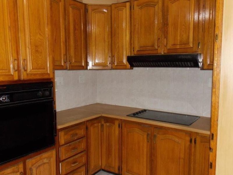 A dated kitchen featuring traditional wooden cabinetry, a built-in oven, electric hob, and extractor fan with a tiled backsplash.