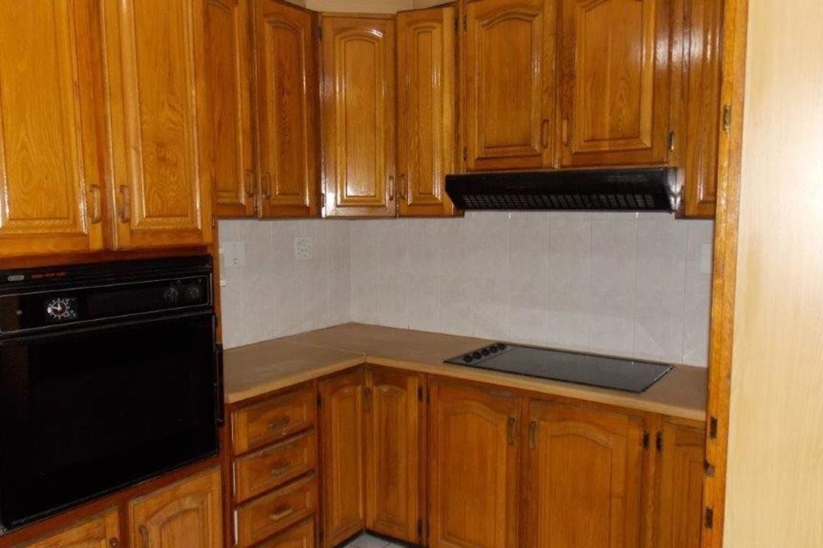 A dated kitchen featuring traditional wooden cabinetry, a built-in oven, electric hob, and extractor fan with a tiled backsplash.