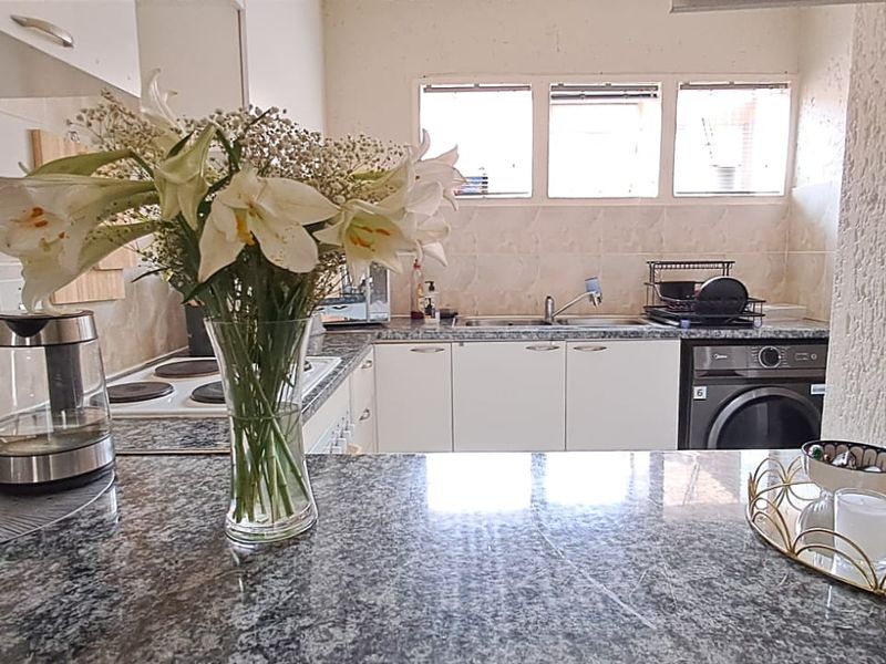 A functional kitchen featuring granite countertops, white cabinetry, a tiled backsplash, and an integrated electric hob with a view towards the sink area.