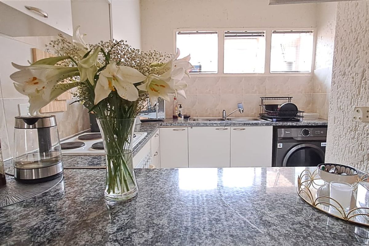 A functional kitchen featuring granite countertops, white cabinetry, a tiled backsplash, and an integrated electric hob with a view towards the sink area.