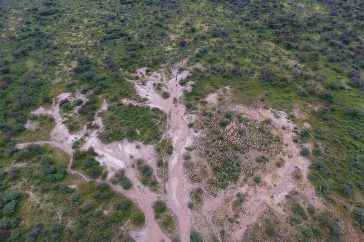 An aerial view of the farm landscape showing natural vegetation, rocky outcrops, and visible soil erosion patterns across the terrain.