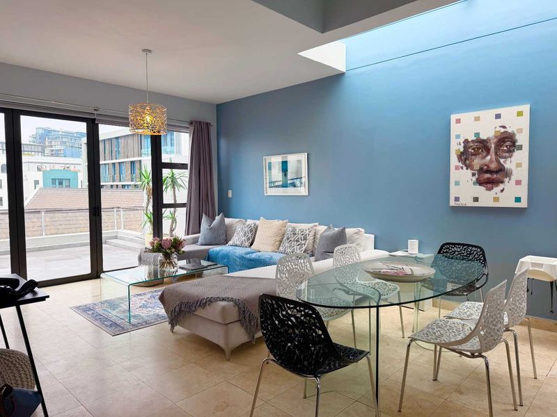 Bright open-plan living and dining area featuring large sliding glass doors leading to a balcony and a modern skylight for natural illumination.