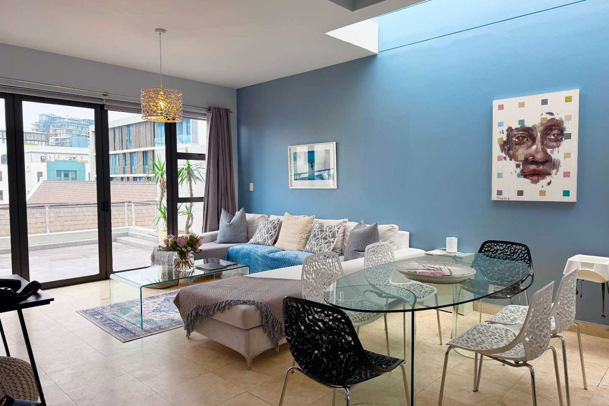 Bright open-plan living and dining area featuring large sliding glass doors leading to a balcony and a modern skylight for natural illumination.
