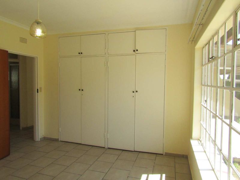A bright, empty bedroom featuring tiled flooring, large steel-framed windows, and extensive built-in cupboard storage.