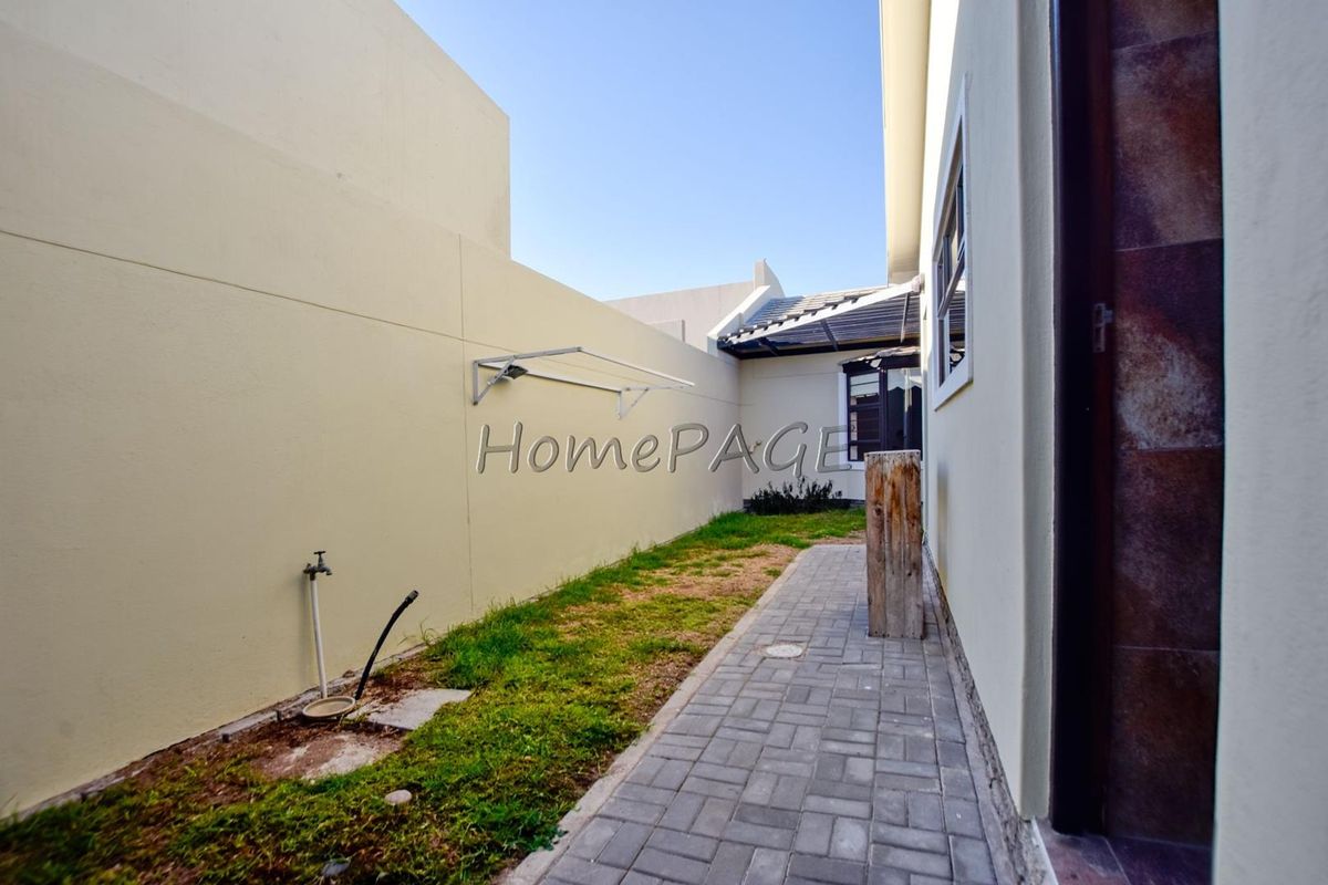 A side exterior area featuring a paved walkway, a small grass section, a wall-mounted drying rack, and an outdoor water tap.