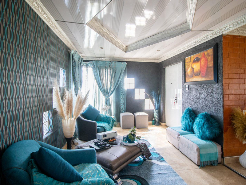 A living room featuring decorative ceiling panels, tiled flooring, and a combination of textured and exposed brick feature walls.