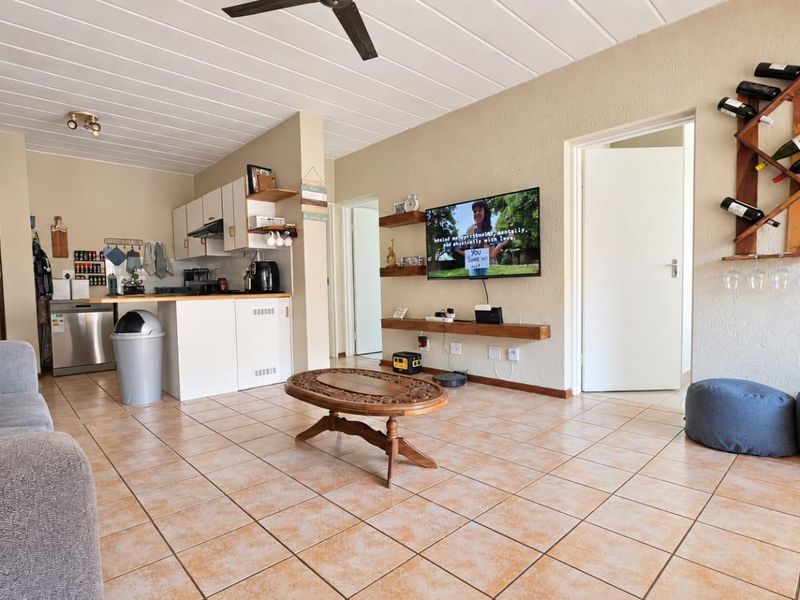 Open-plan living area featuring a functional kitchen with cabinetry, tiled flooring throughout, and a ceiling fan, creating a versatile and connected living space.