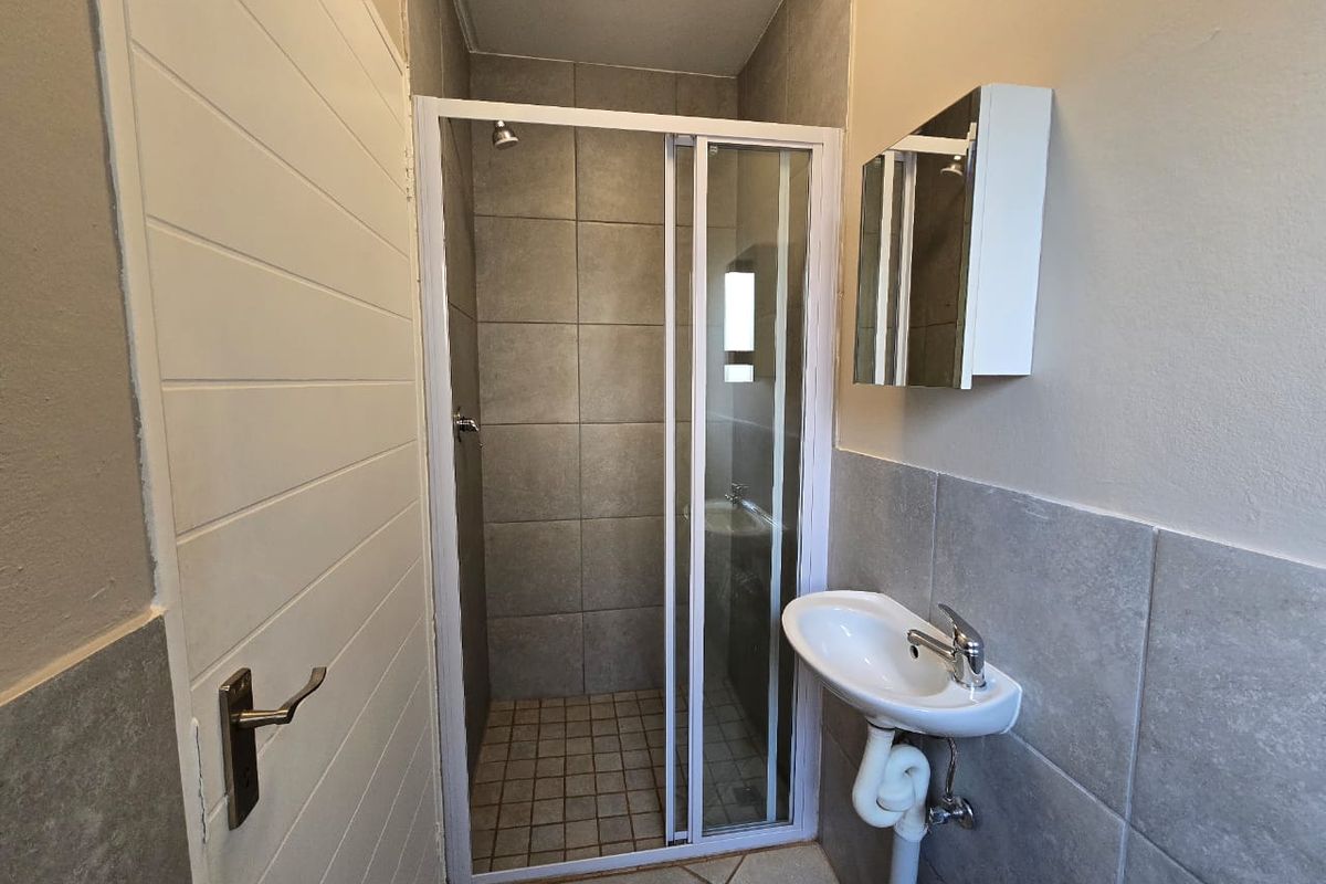 A compact, functional bathroom featuring a glass-enclosed shower, wall-mounted basin with mixer tap, and neutral tiled finishes.