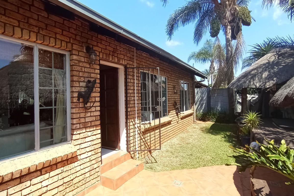 Rear exterior view of the townhouse featuring a face brick facade, tiled patio area, and a thatched lapa in the garden.