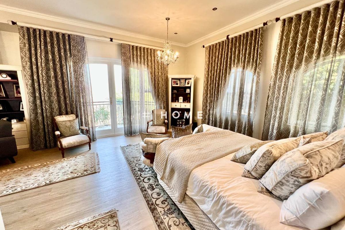 Spacious bedroom featuring light wood-look flooring, elegant chandelier lighting, and double doors opening to a private balcony with ample natural light.