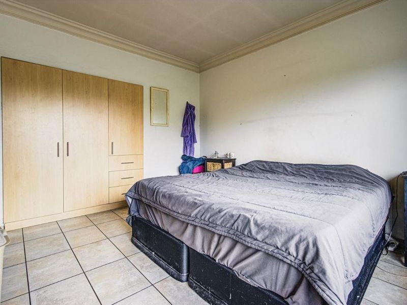 A bedroom featuring tiled flooring, a built-in wardrobe, and coved ceiling detailing, offering a functional space with potential for cosmetic updates.