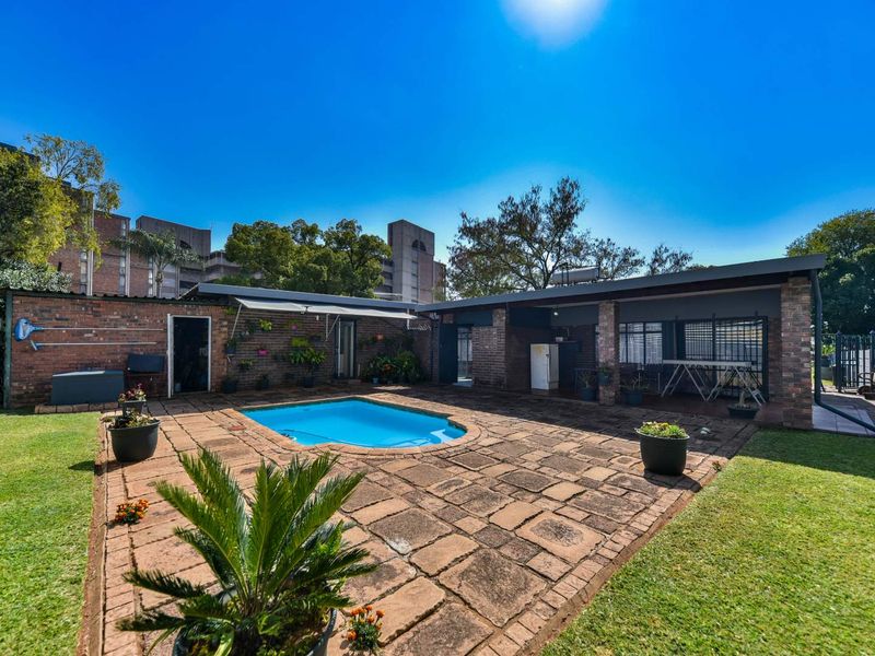 Outdoor pool area featuring a paved patio, covered entertainment space, and surrounding lawn, ideal for relaxation and outdoor gatherings.