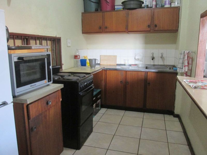 A functional kitchen featuring dated laminate cabinetry, a stainless steel sink, tiled backsplash, and ceramic floor tiles, offering potential for modernization.