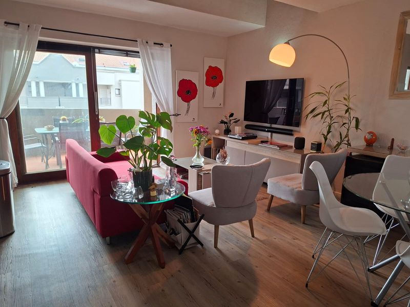 A well-lit living room featuring laminate flooring and a large sliding glass door that provides access to an outdoor balcony area.