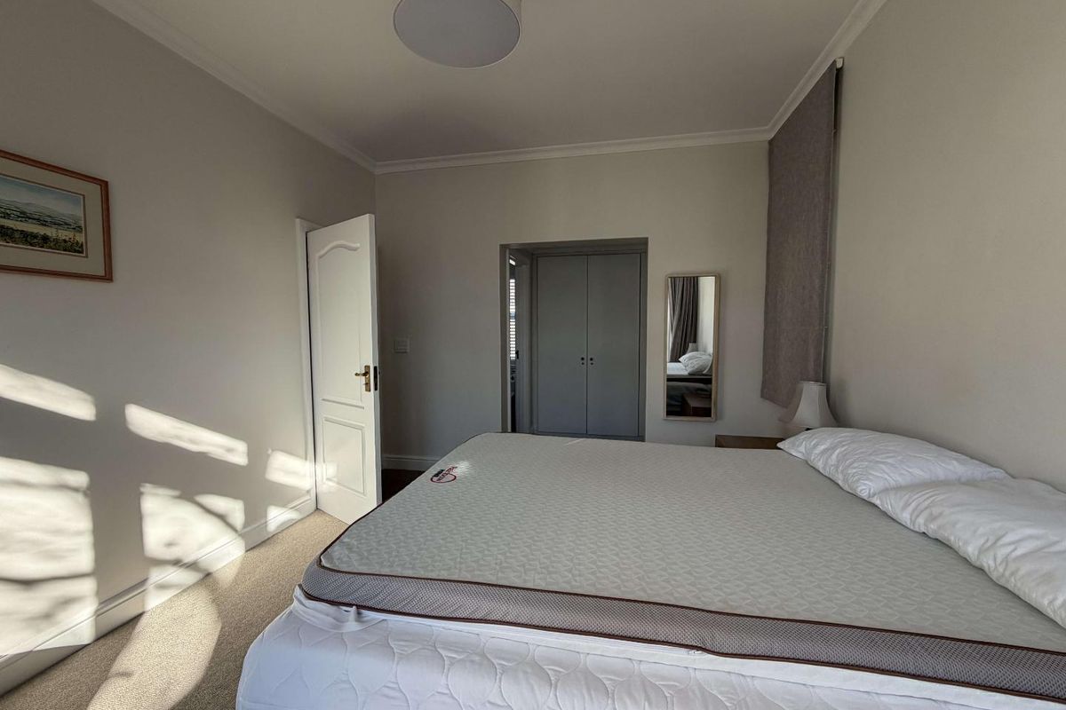 A well-lit bedroom featuring neutral wall tones, carpeted flooring, and built-in cupboard storage.