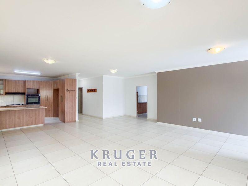 Spacious open-plan living area featuring a modern kitchen with built-in cabinetry, oven, and hob, finished with neutral tiled flooring throughout.