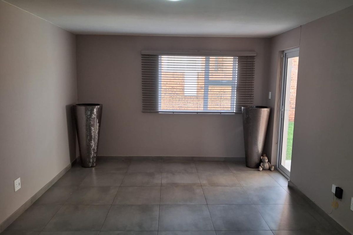 A neutral-toned living area featuring large format floor tiles, a window with fitted blinds, and a glass door providing access to the exterior.