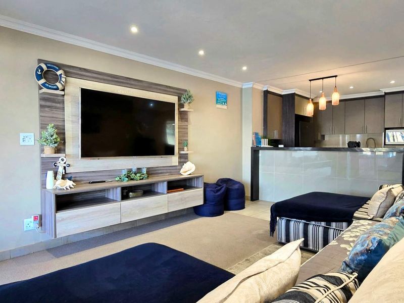 Open-plan living area featuring a modern built-in media unit and a functional kitchen with a breakfast bar island and contemporary cabinetry.