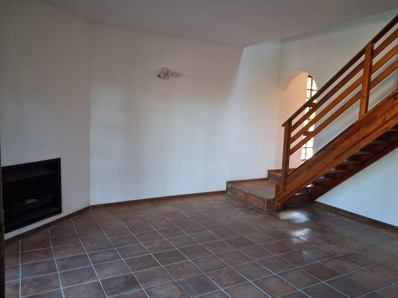 Spacious living area featuring tiled flooring, a built-in fireplace, and a wooden staircase leading to the upper level.