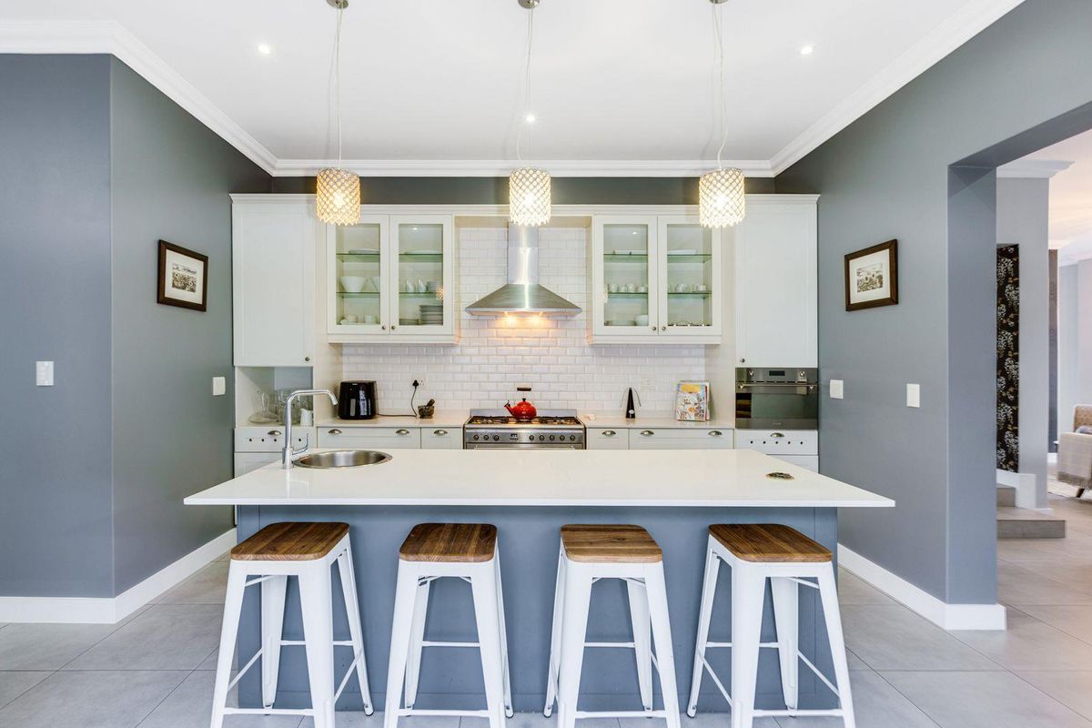 Modern kitchen featuring a central island with a prep sink, white cabinetry, subway tile backsplash, stainless steel extractor fan, and built-in oven.