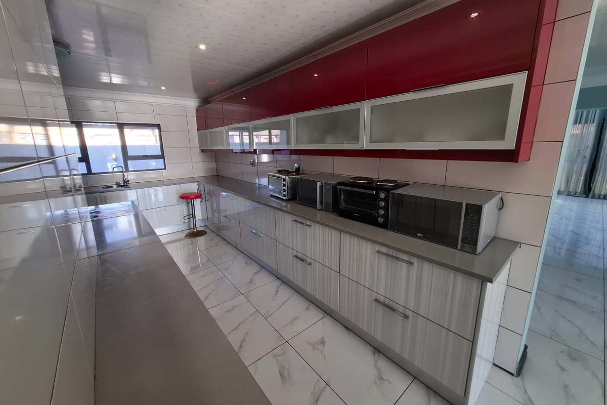 A modern kitchen featuring high-gloss red upper cabinetry, light wood-grain lower cabinets, stone countertops, and large format floor tiles.