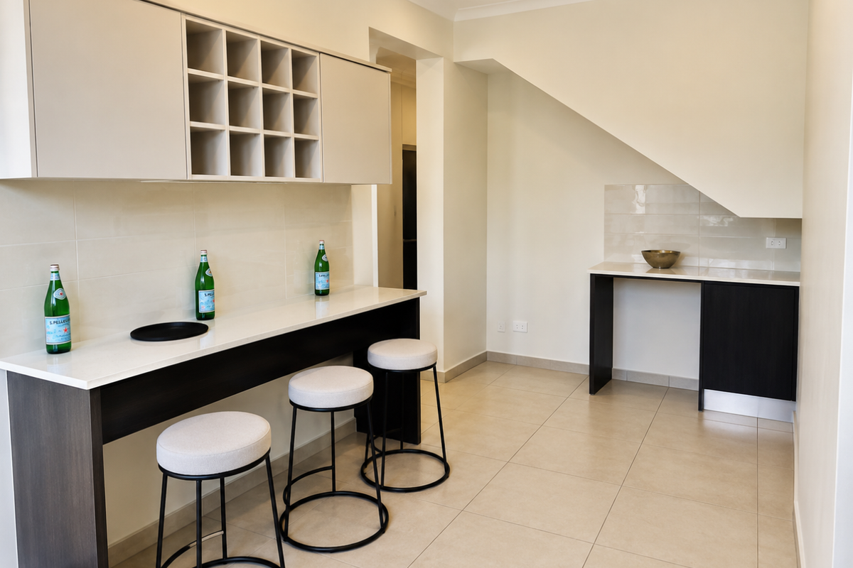 A modern kitchen area featuring sleek built-in cabinetry, stone countertops, a tiled backsplash, and neutral floor tiles, offering a clean and functional workspace.