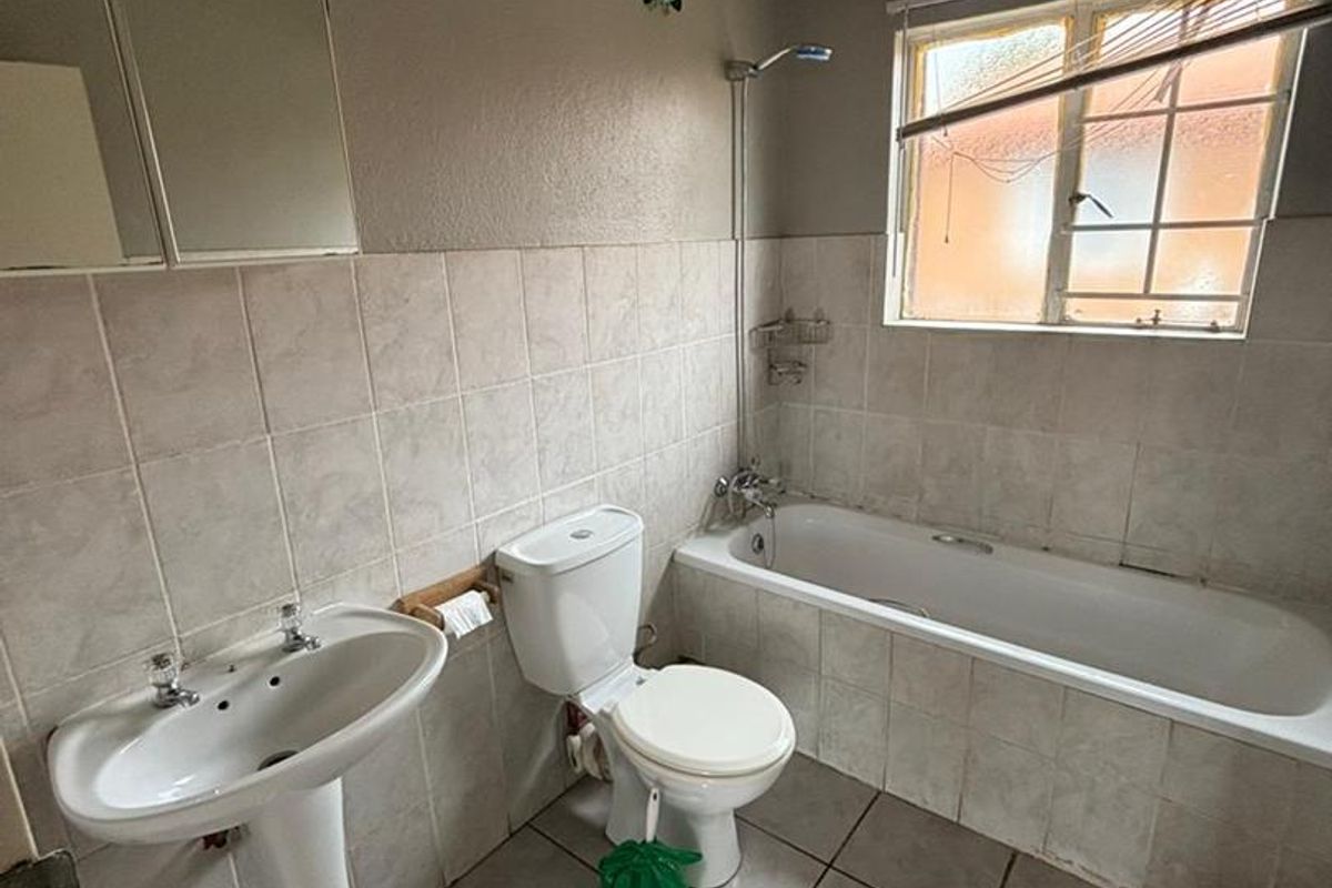 A dated bathroom featuring a pedestal basin, standard toilet, and a bathtub with a shower mixer, finished with neutral wall and floor tiles.