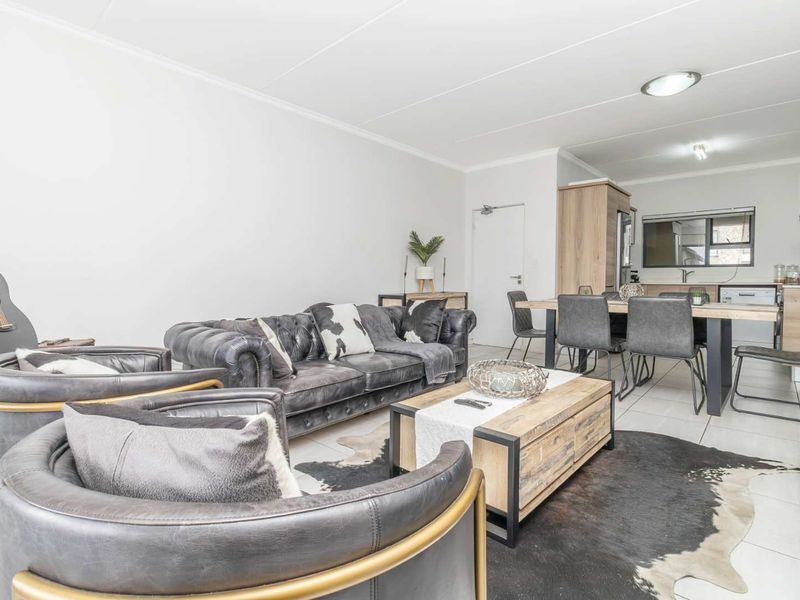 A bright open-plan living and dining area featuring tiled flooring and a modern kitchen with built-in cabinetry and integrated appliances.