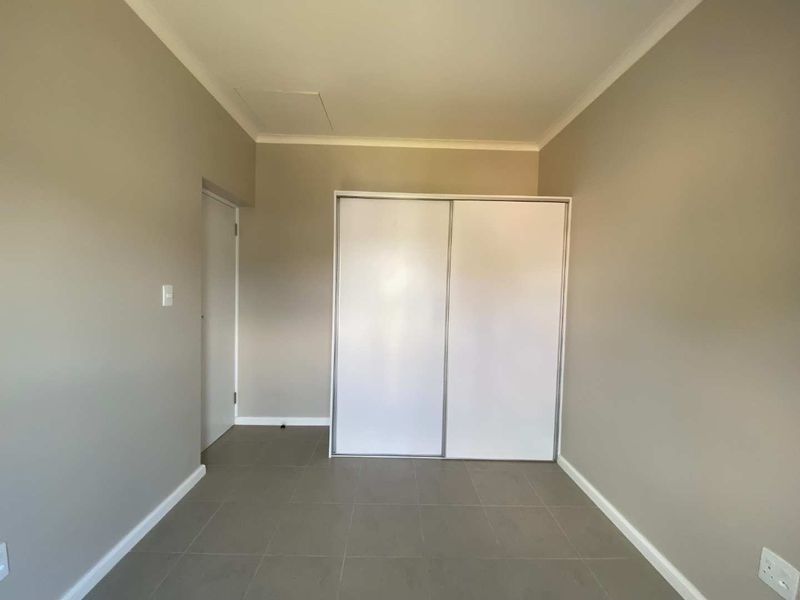 A clean, empty bedroom featuring neutral wall tones, tiled flooring, and a built-in sliding door wardrobe.