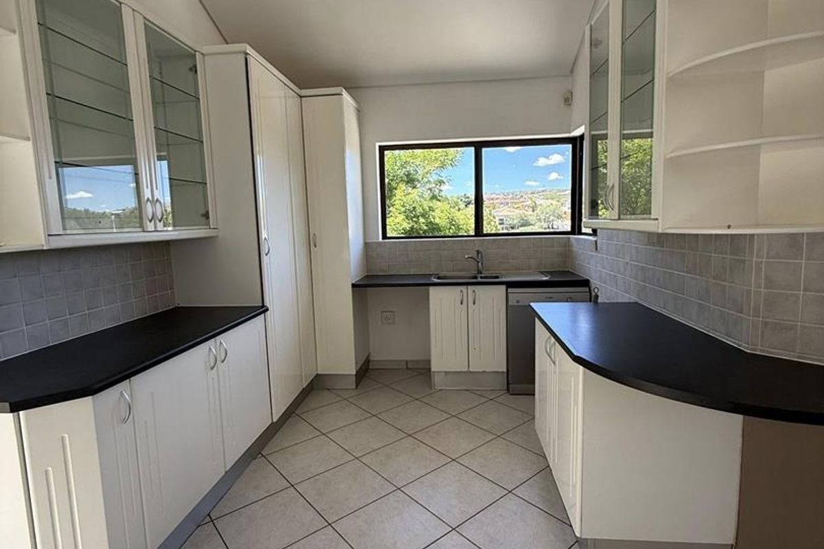 A functional kitchen featuring white cabinetry, dark countertops, tiled flooring, and a window providing natural light and views.